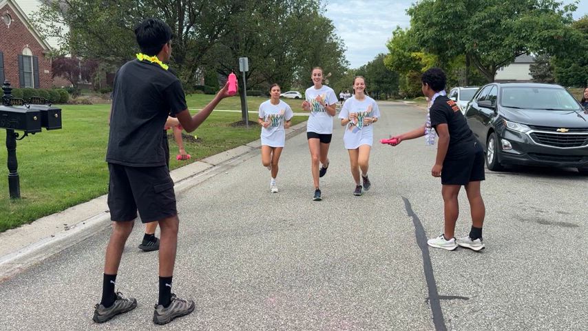 A lively montage of past Color My World 5K events showing participants running and walking through colorful powder, smiling and laughing with friends and family. Text on screen reads: 