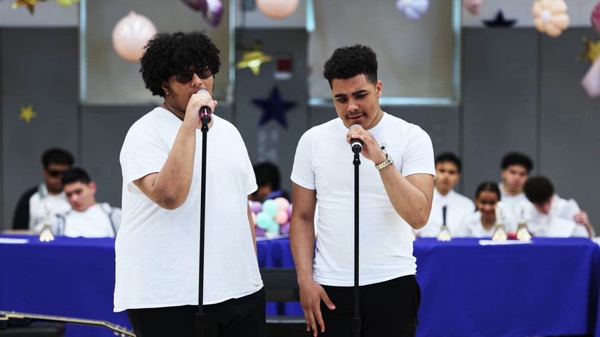 2 boys sing into microphones in the middle of a gymnasium 