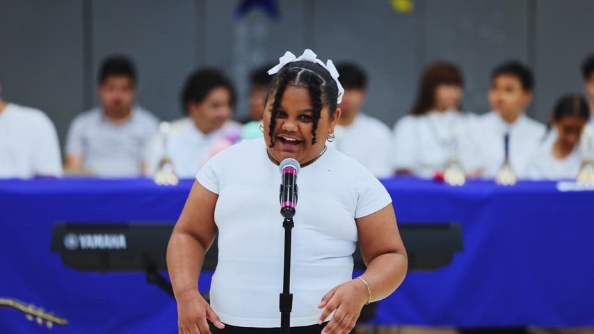 A girl sings into a microphone in a gymnasium 
