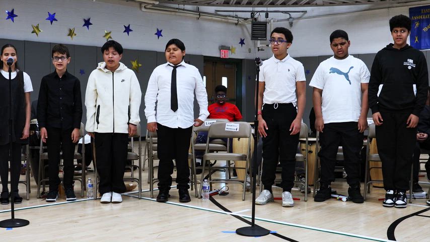 a group of students stand at their chairs in a gymnasium and sing 