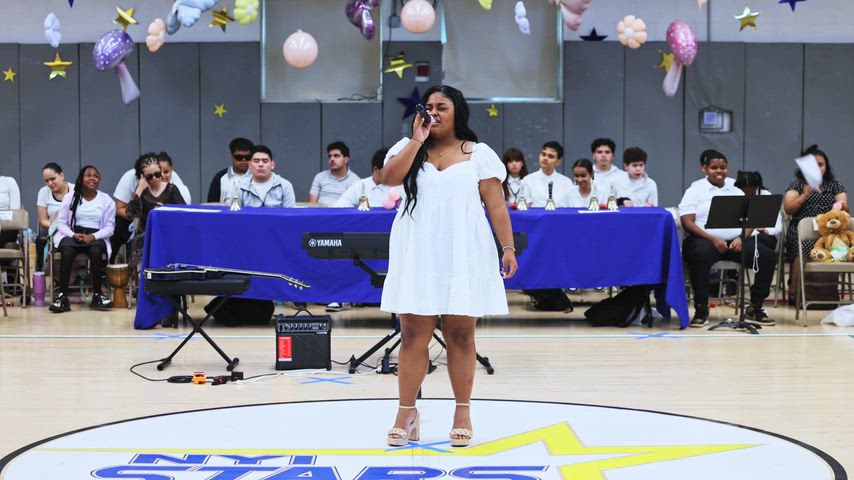 A girl sings into a microphone in the middle of a gymnasium 
