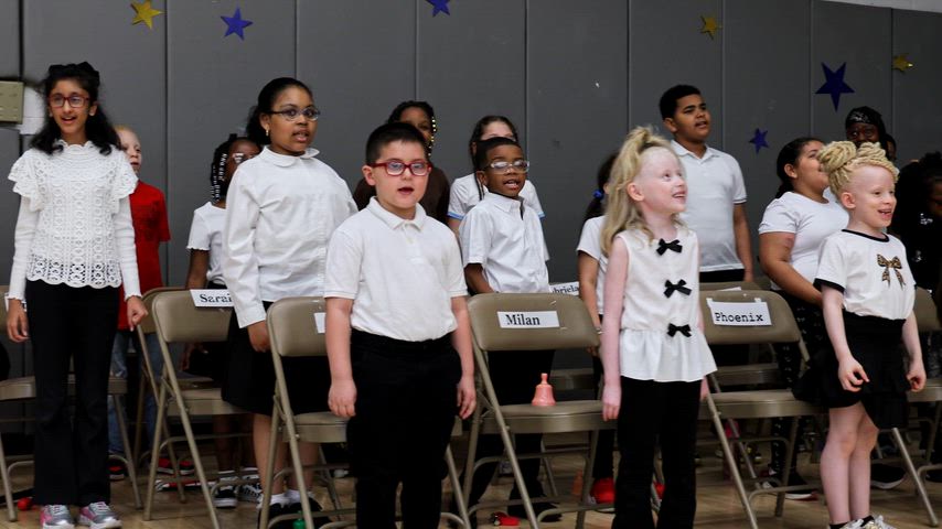 A group of young students all sing in the corner of a Gymnasium 