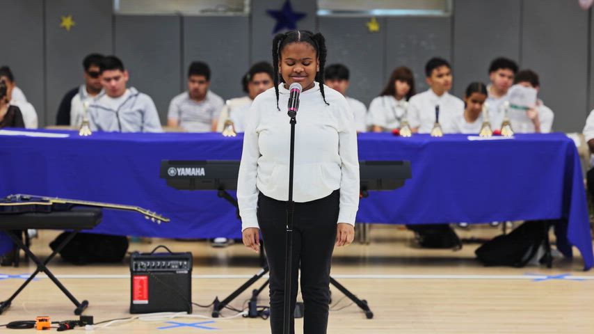 a girl sings into a microphone in a gymnasium 