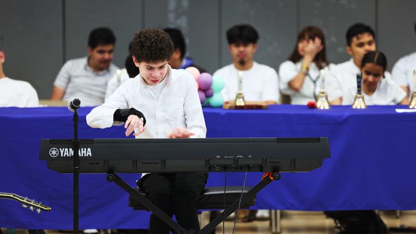 a boy plays a piano in the middle of a gymnasium 