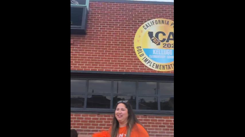 video showing students in matching school spirit pumpkin organge greeting everyone in the morning